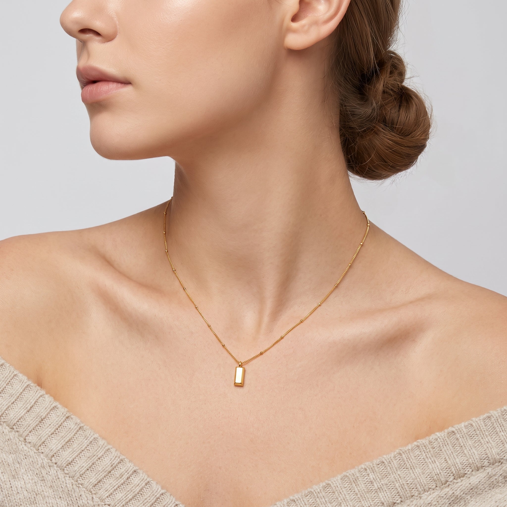 Gold bar pendant necklace on a beaded chain, worn at the neck