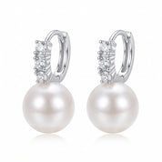 Pair of silver pearl drop huggie earrings on white