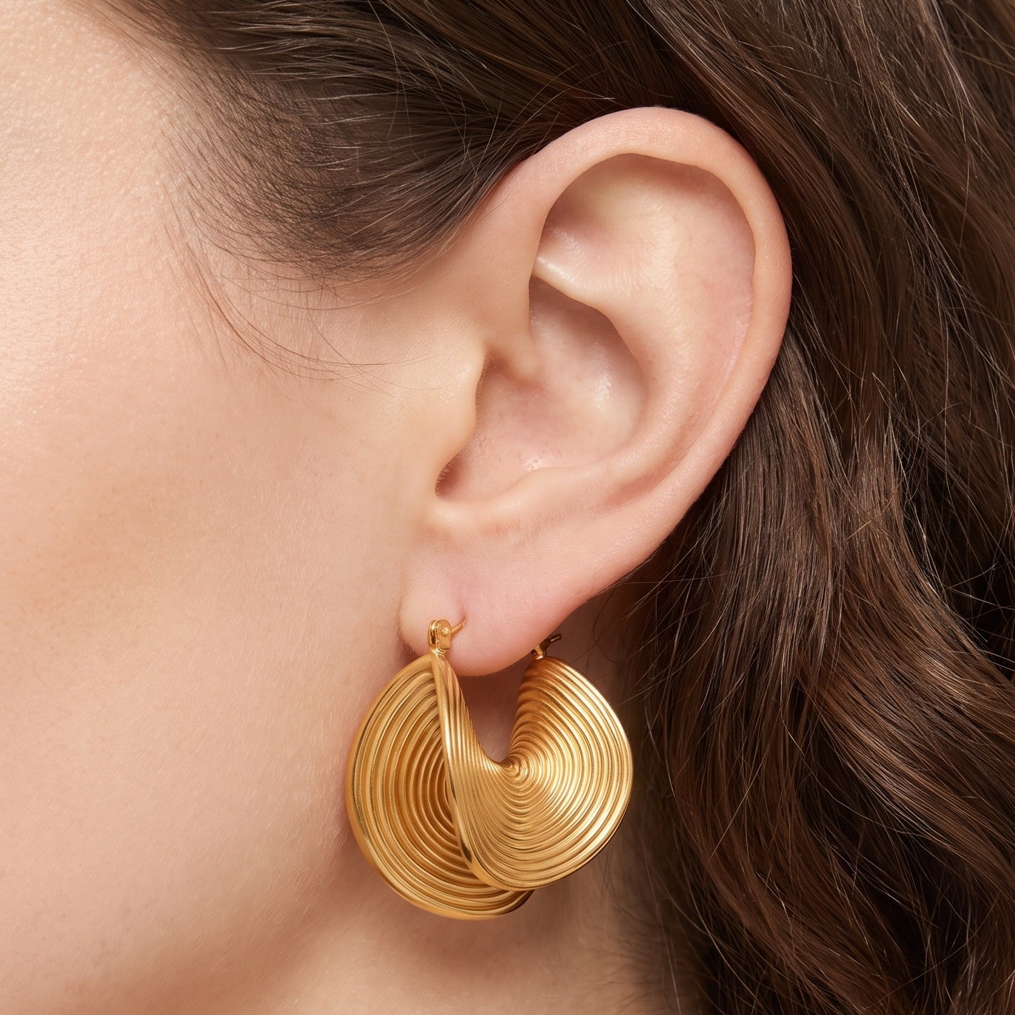 Gold spiral hoop earrings with a folded ribbed design on the ear