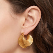 Gold spiral hoop earrings with a folded ribbed design on the ear