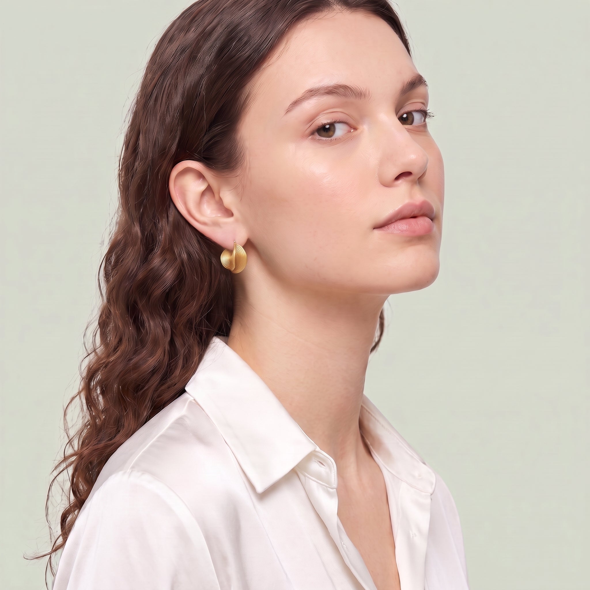 Gold spiral hoop earring worn with a white silk shirt