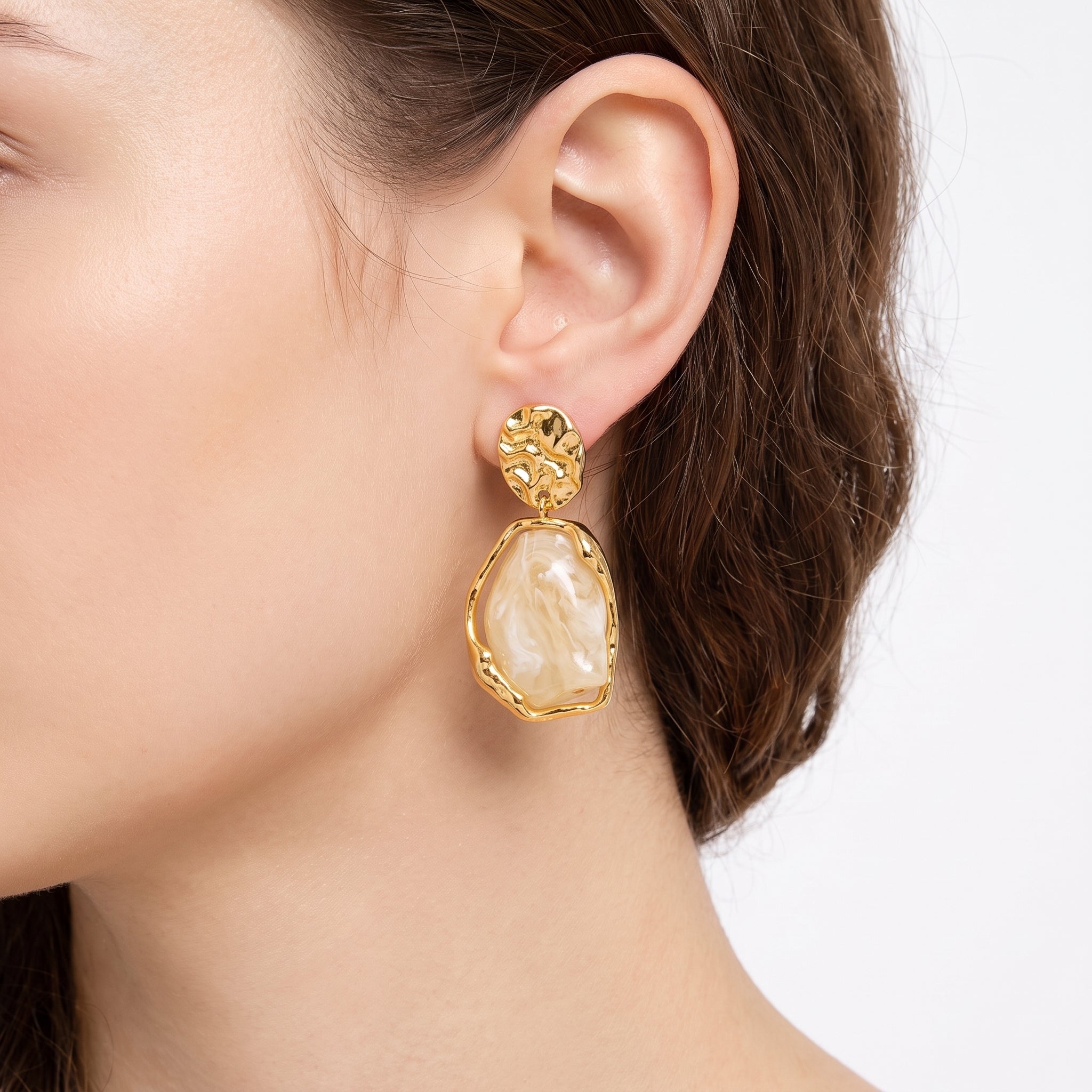 Gold and cream resin drop earring with hammered disc stud, worn