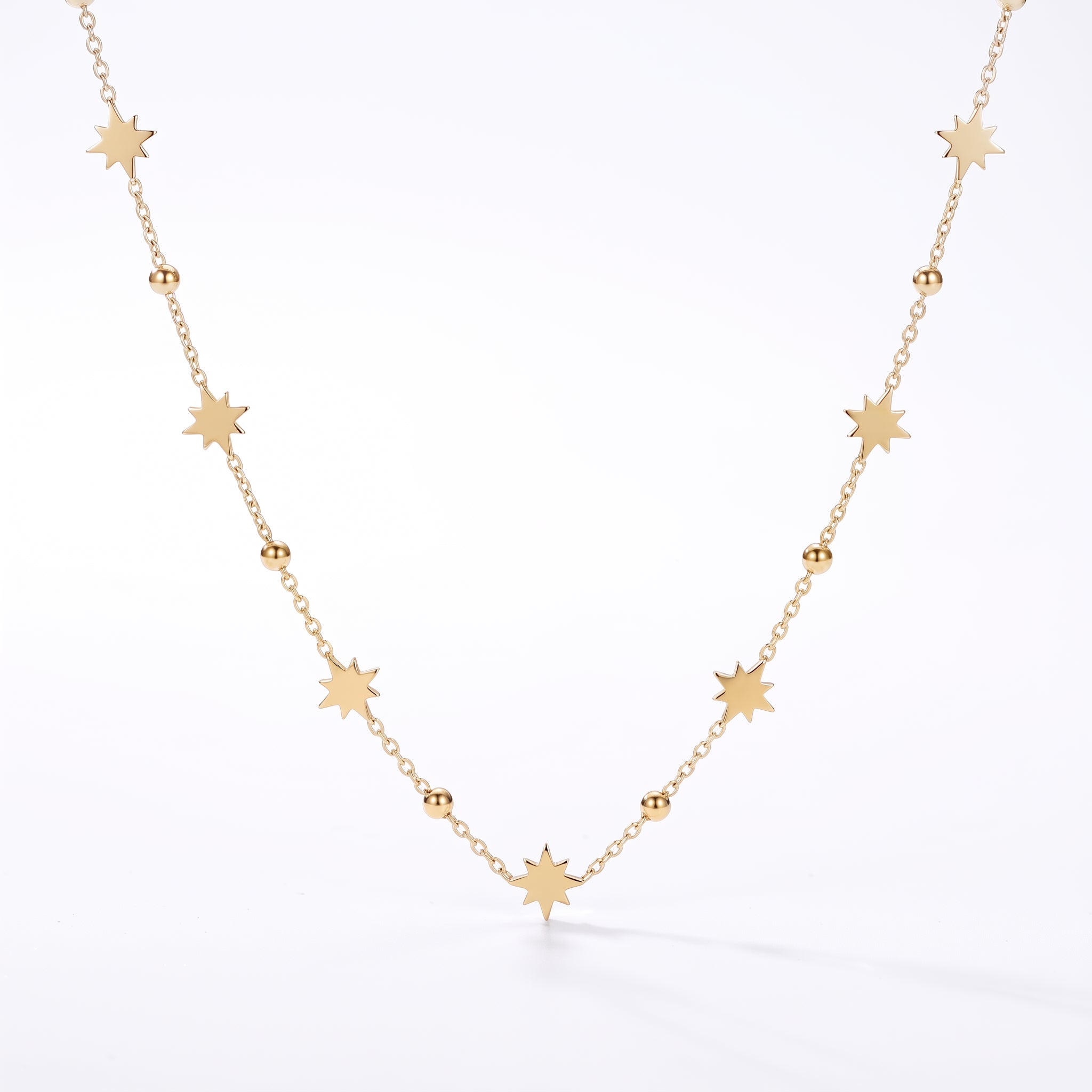 Gold star station necklace hanging in a V on a white background