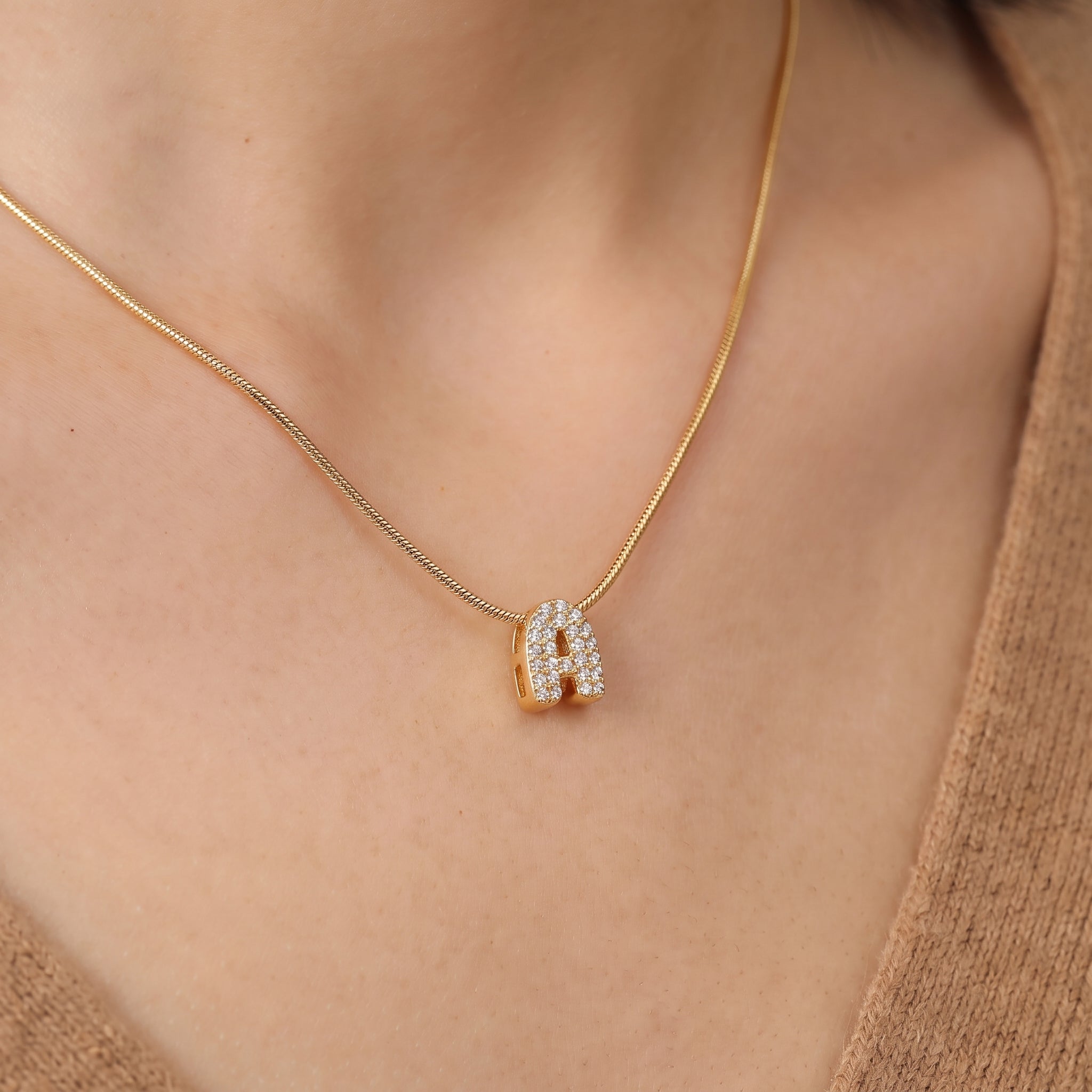 Close-up of the gold bubble letter necklace's pavé A on skin