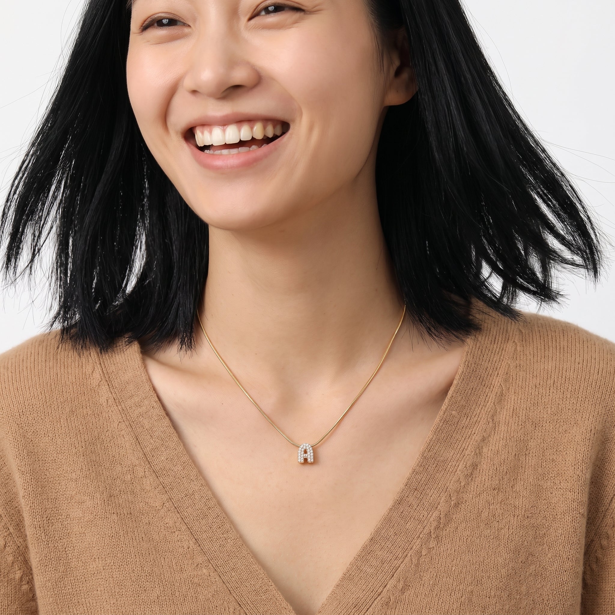 Gold bubble letter necklace worn with a camel V-neck sweater