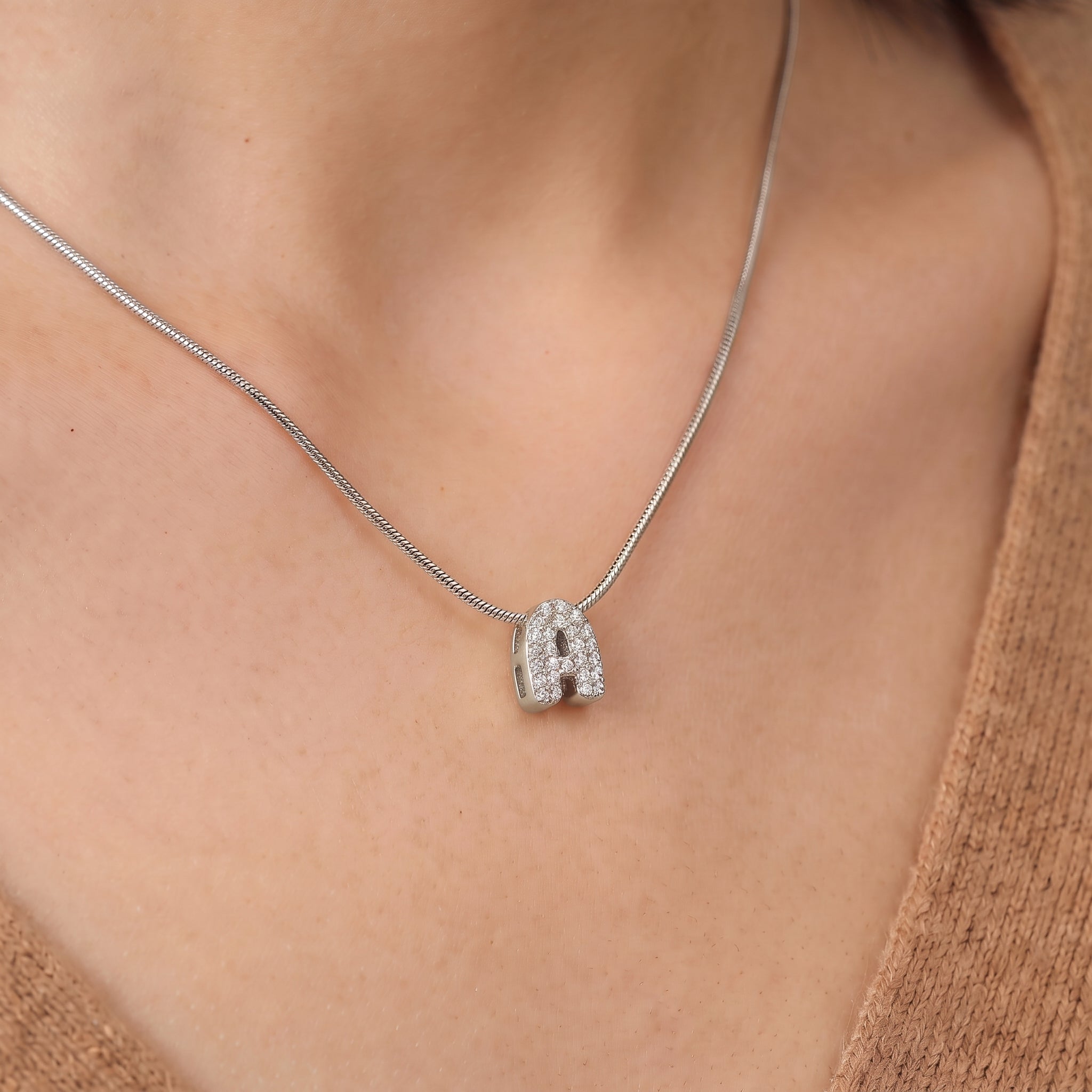 Close-up of the silver bubble letter necklace's pavé A on skin