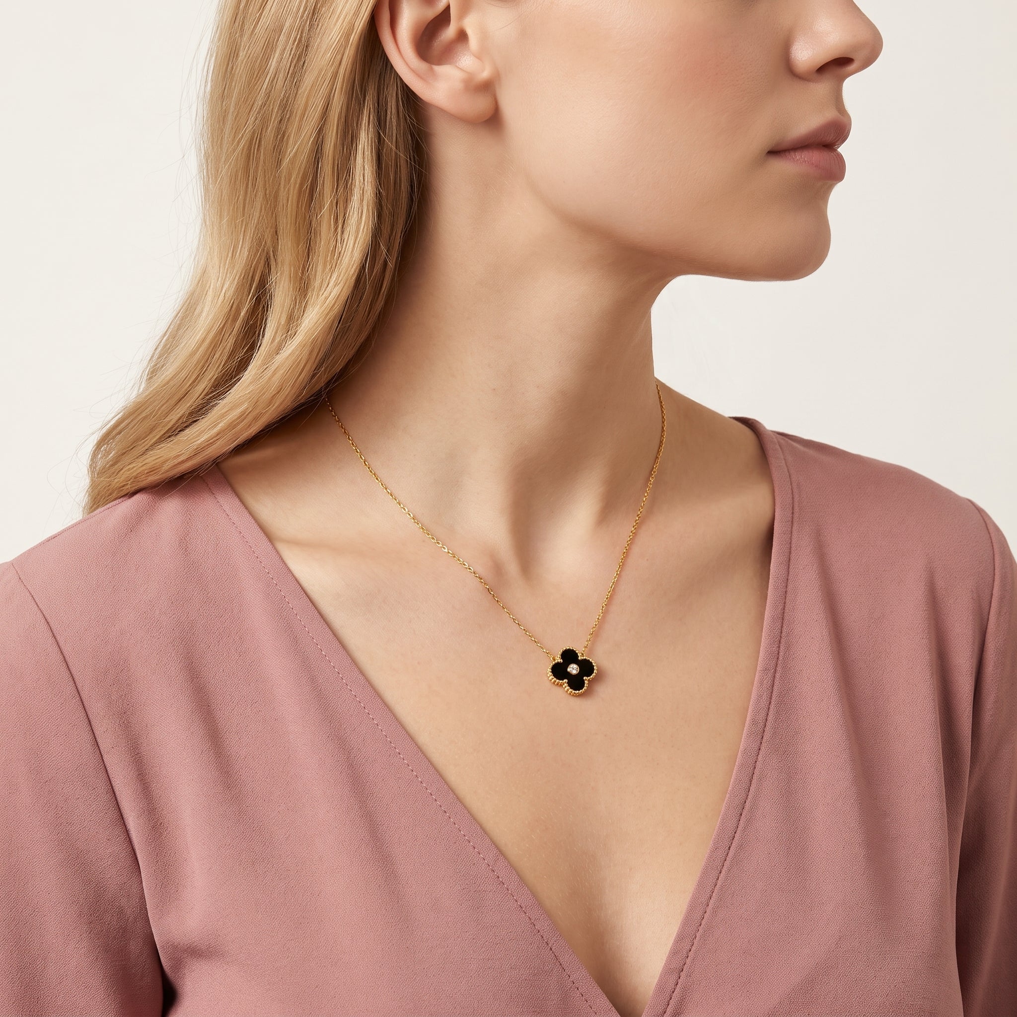Gold black clover necklace worn with a pink wrap top, side view