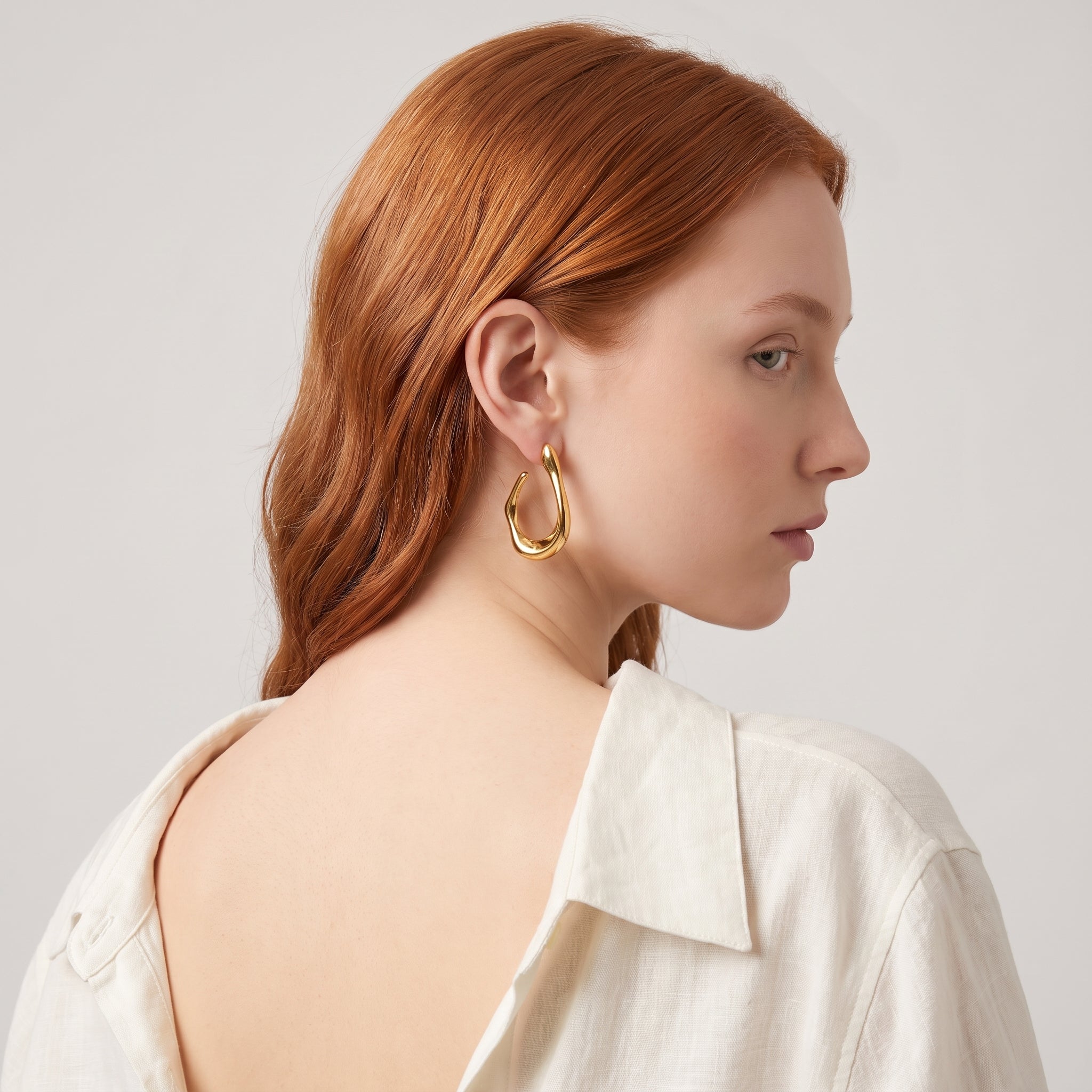 Gold chunky open hoop earring seen over the shoulder