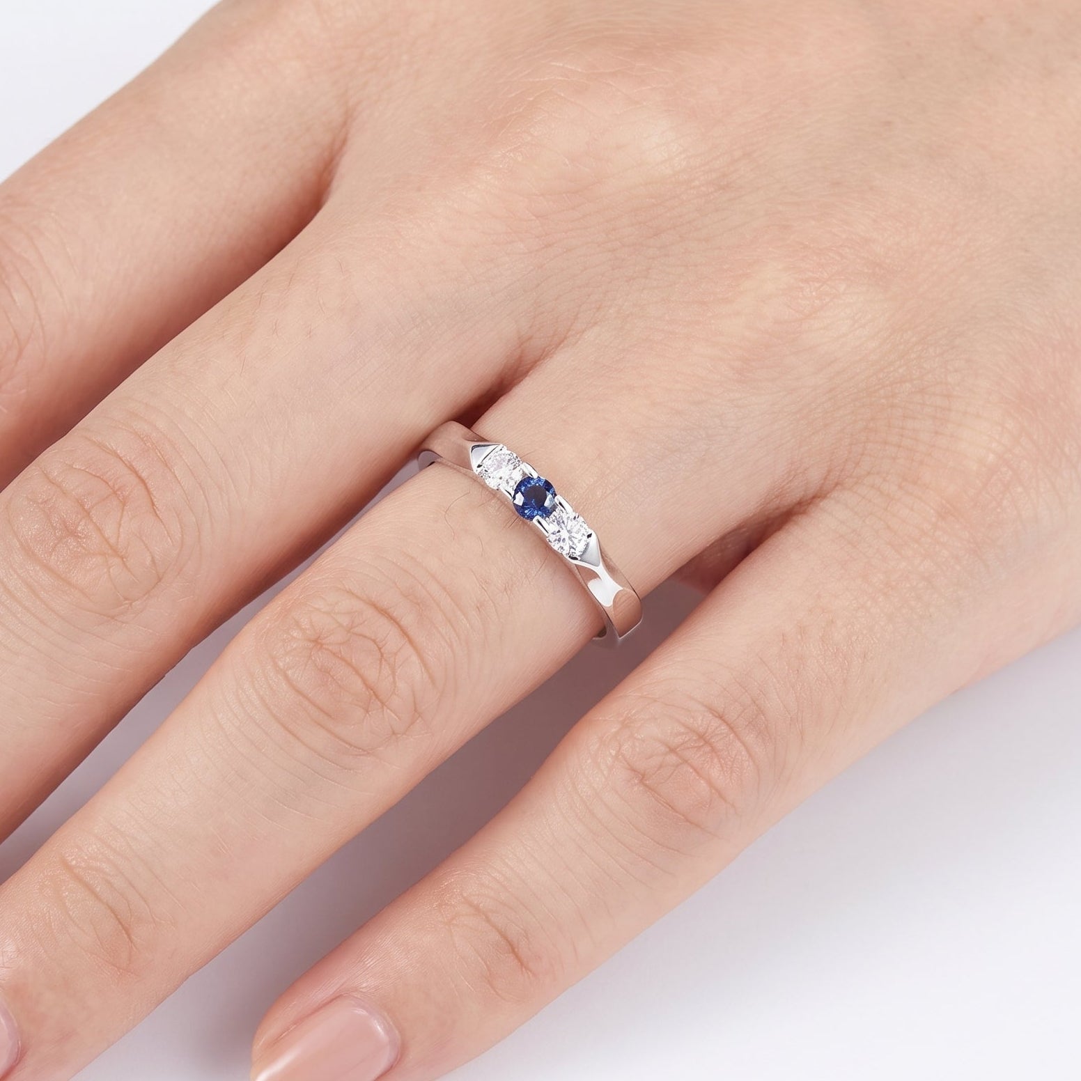 Silver three stone ring with a deep blue center stone on a hand
