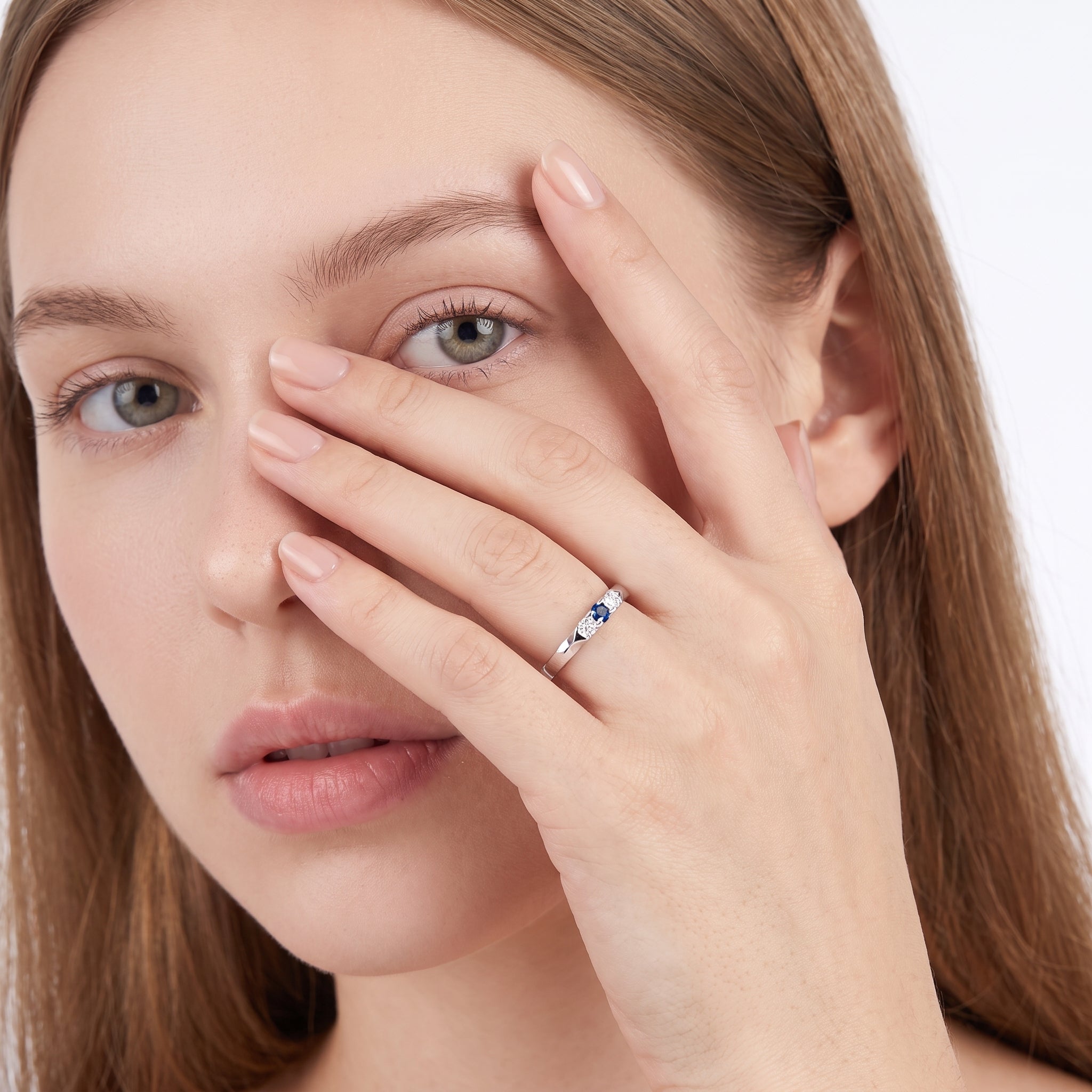 Hand across the face wearing a silver blue three stone ring