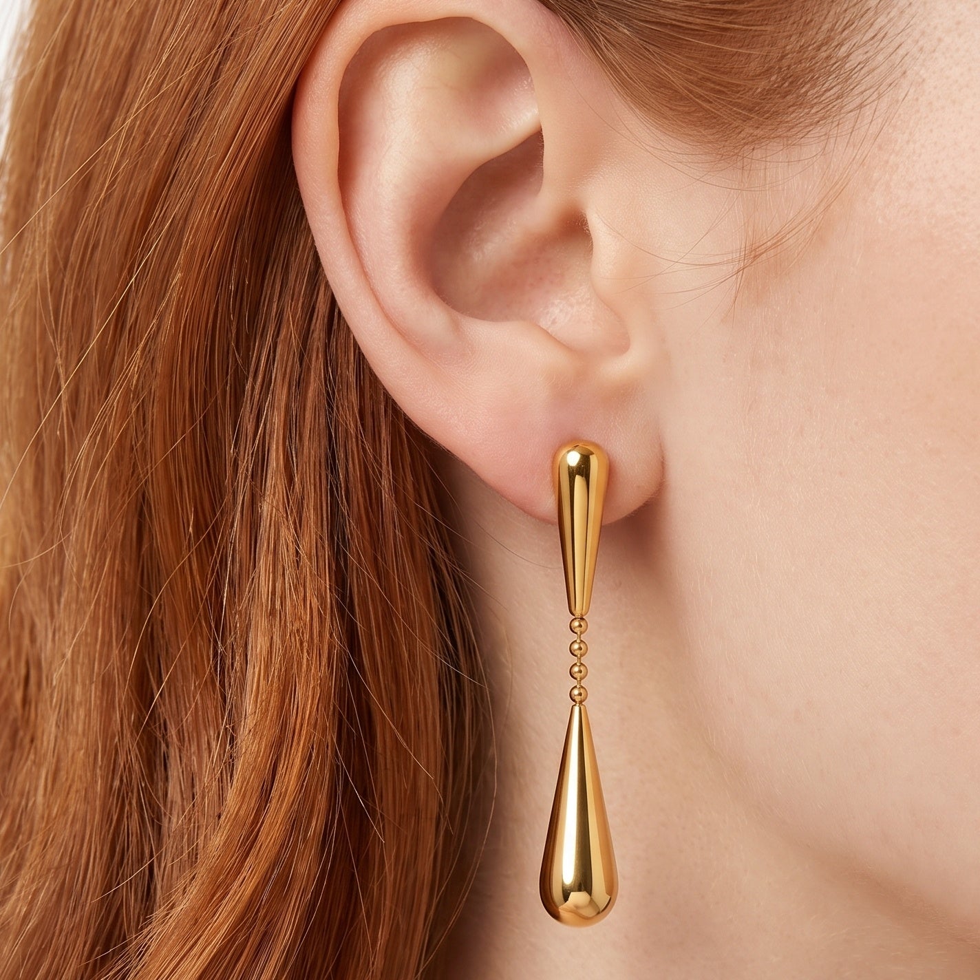 Gold teardrop drop earring on a bead chain, worn on the ear