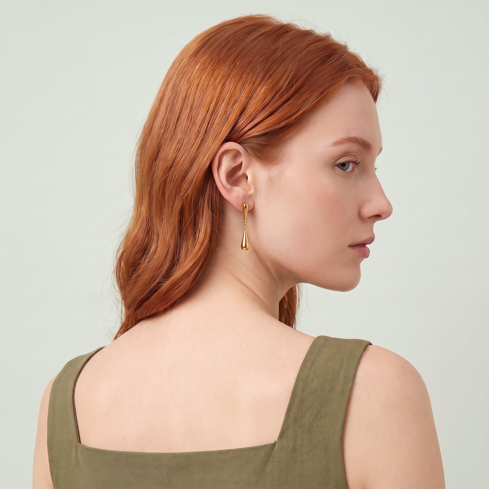 Gold teardrop earring worn with an over-the-shoulder glance