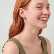 Gold teardrop earring worn while laughing, olive green dress