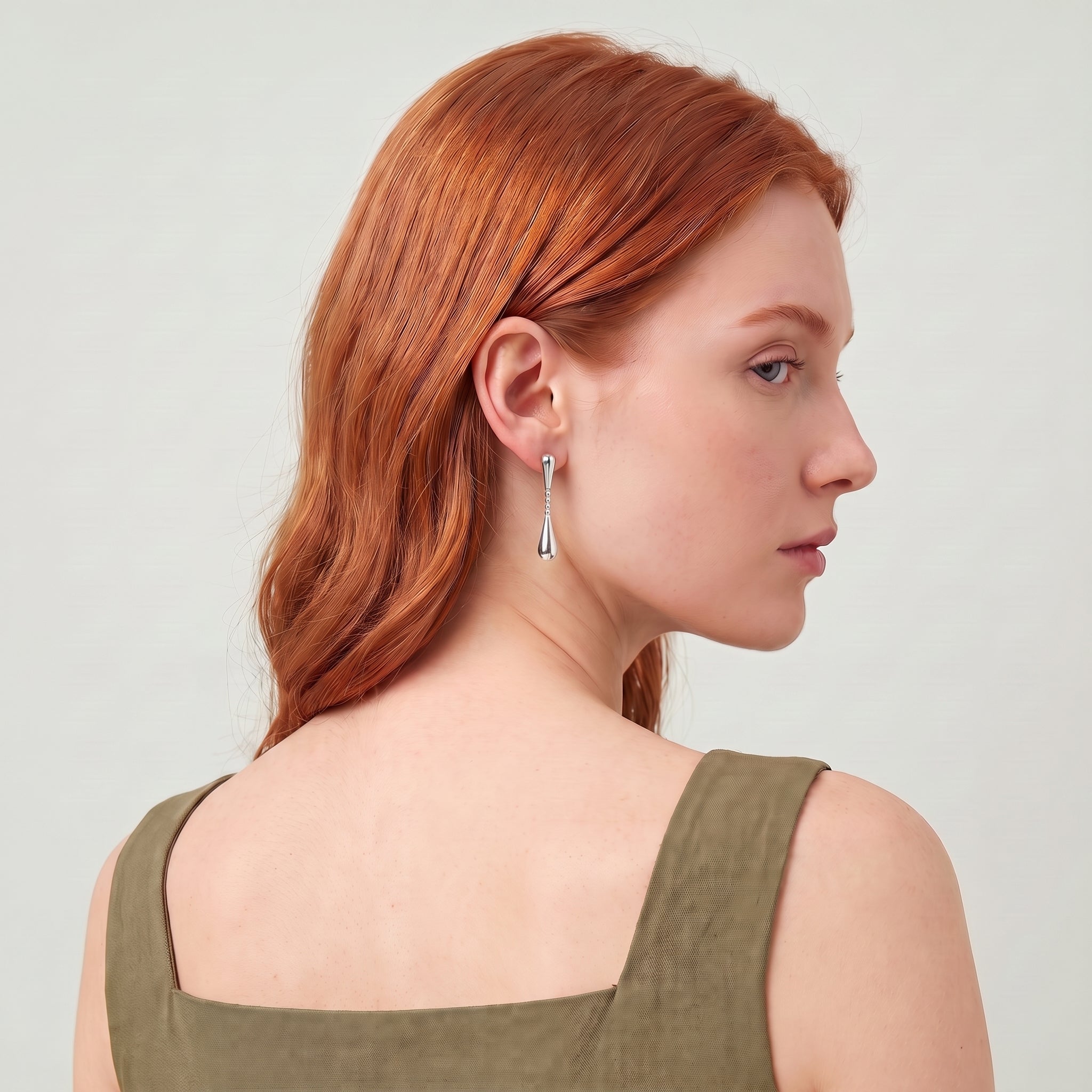 Silver teardrop earring worn with an over-the-shoulder glance