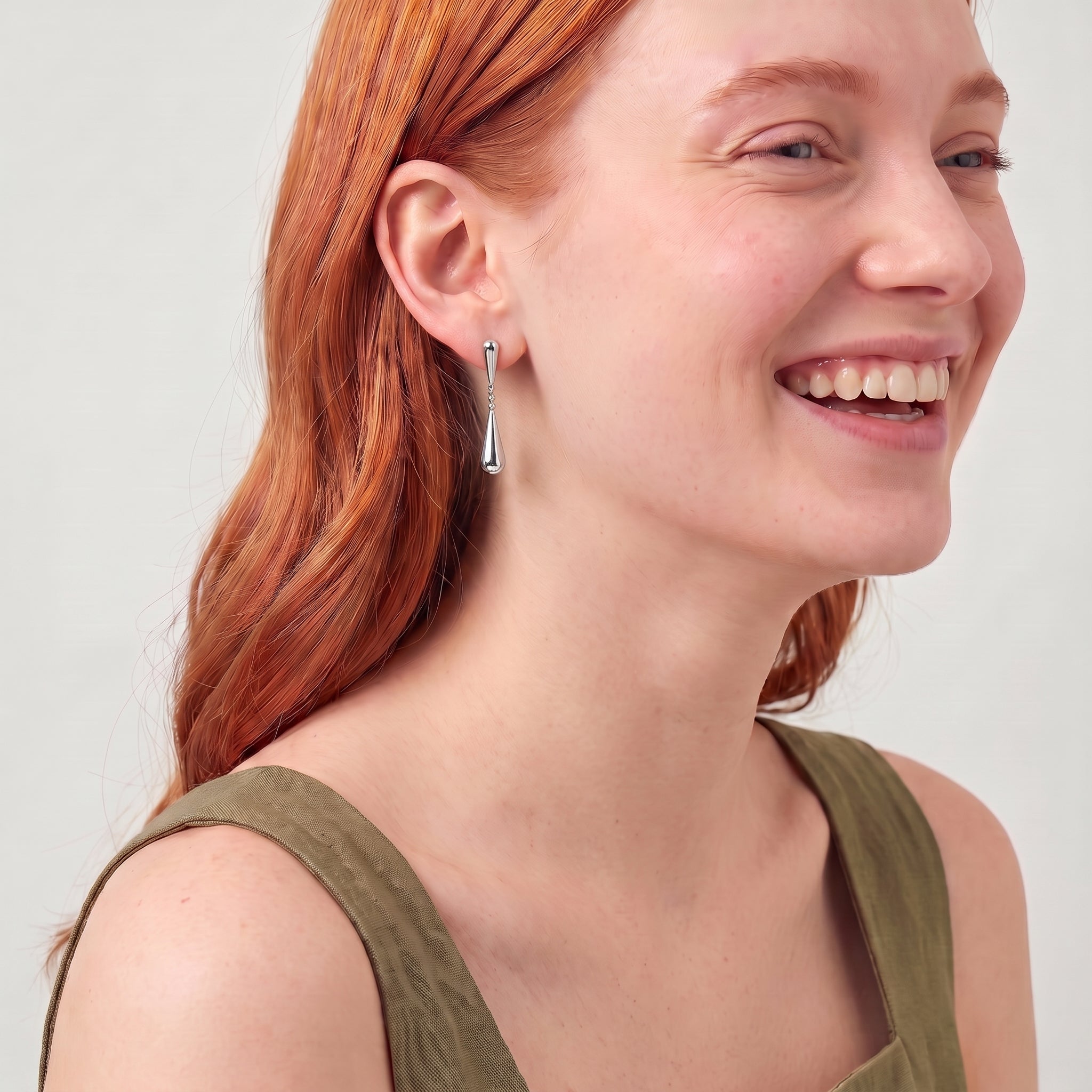 Silver teardrop earring worn while laughing, olive green dress