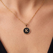 Gold initial disc necklace with a black letter K pendant on skin