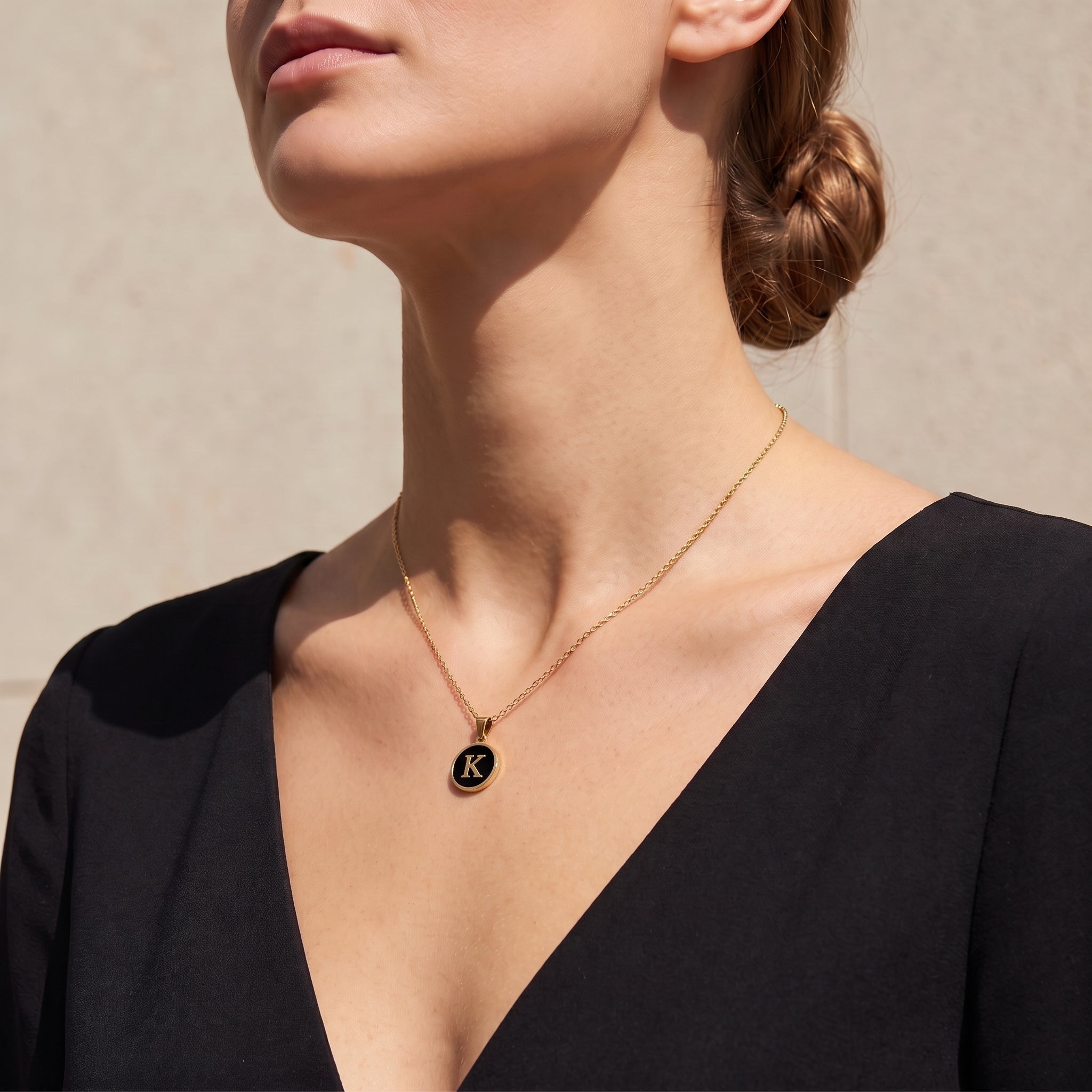 Perrine black initial disc necklace at the collarbone in soft sunlight