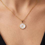 Gold initial disc necklace with a mother of pearl letter K pendant on skin