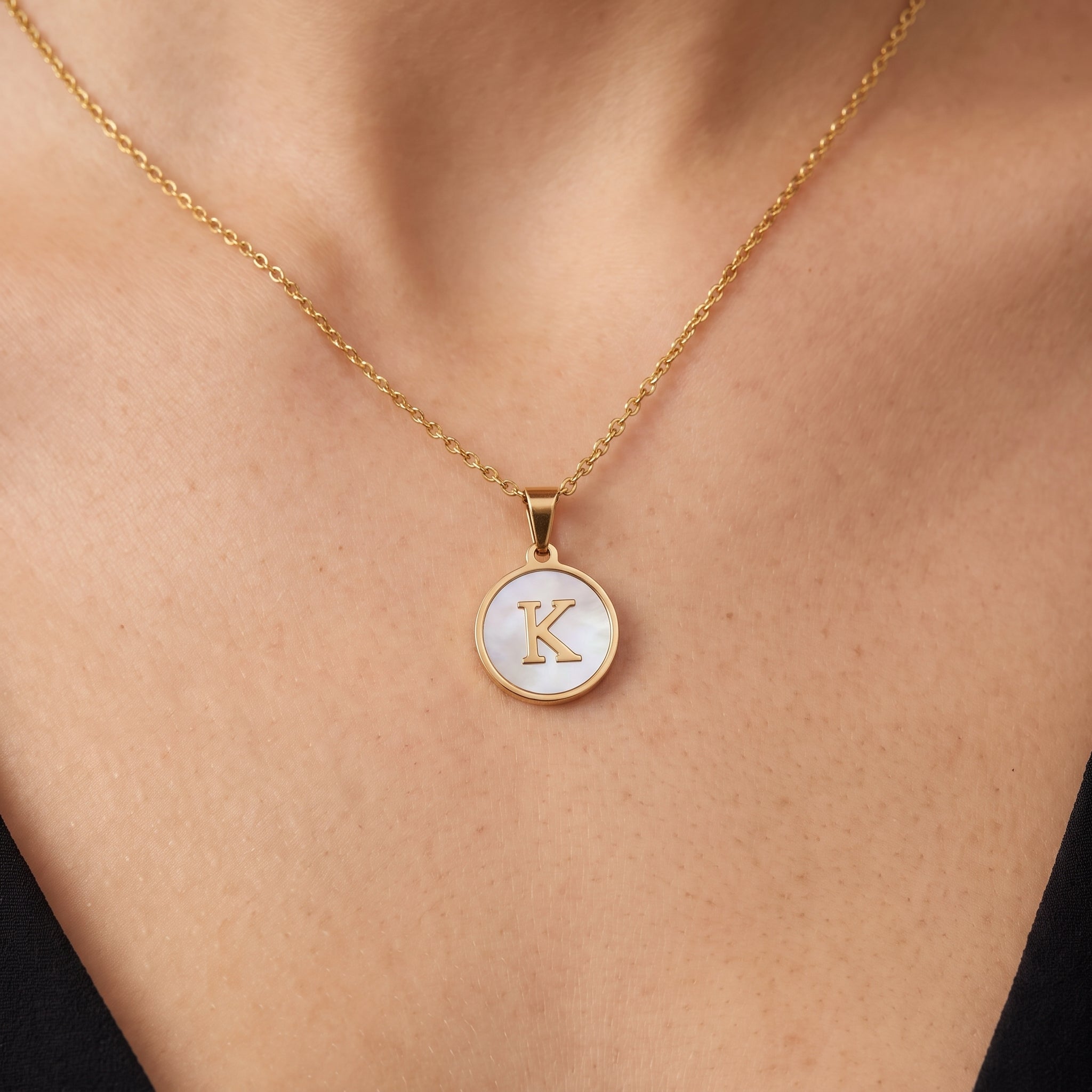 Gold initial disc necklace with a mother of pearl letter K pendant on skin