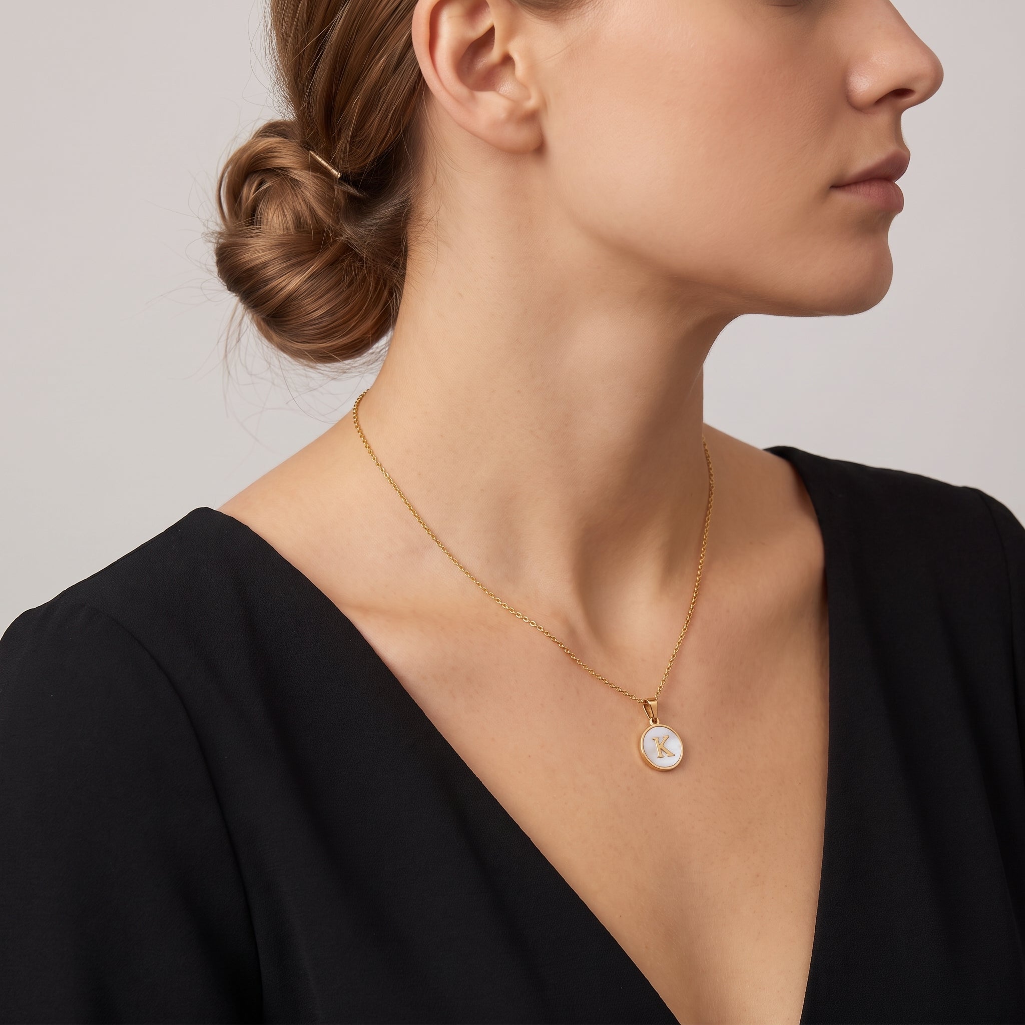 Perrine gold initial disc necklace, side profile with hair in a low bun