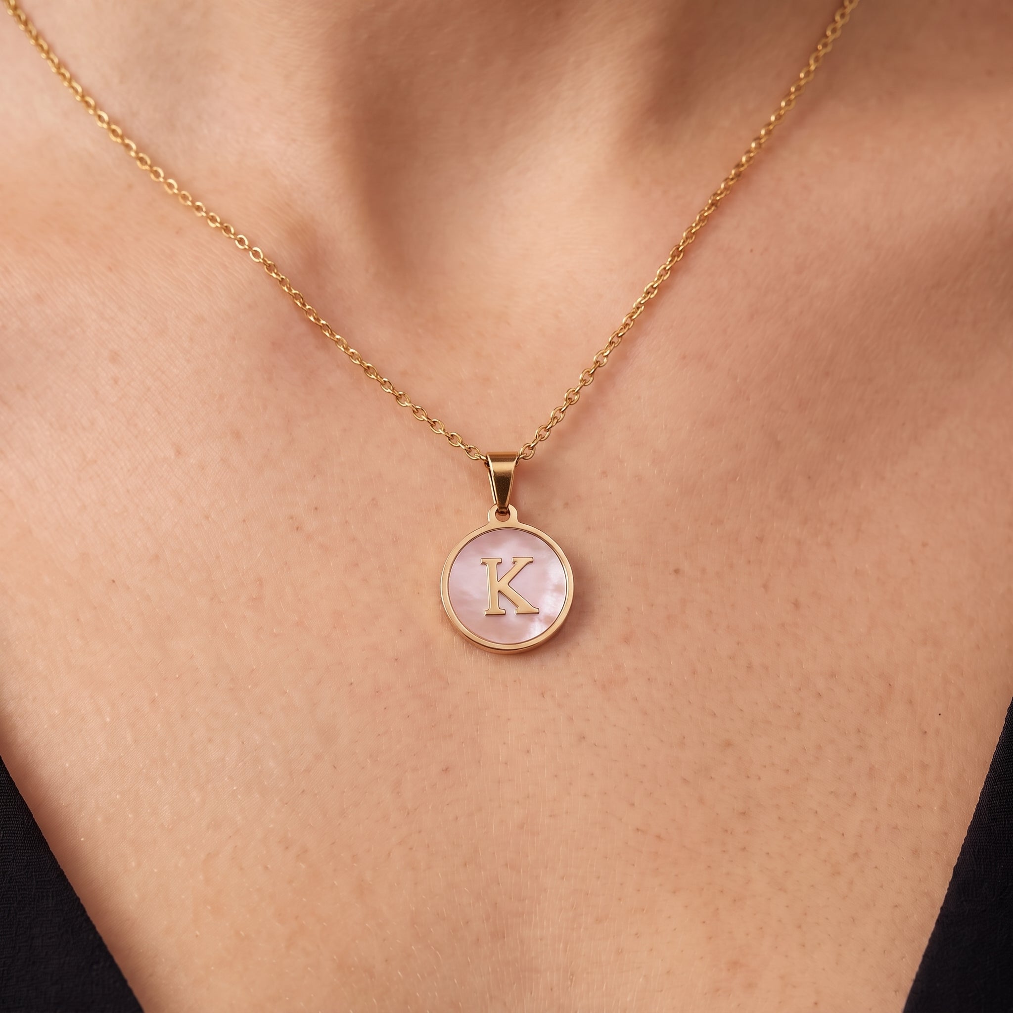 Gold initial disc necklace with a pink mother of pearl letter K pendant on skin