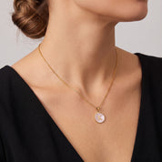 Perrine pink initial disc necklace worn with a black V-neck dress