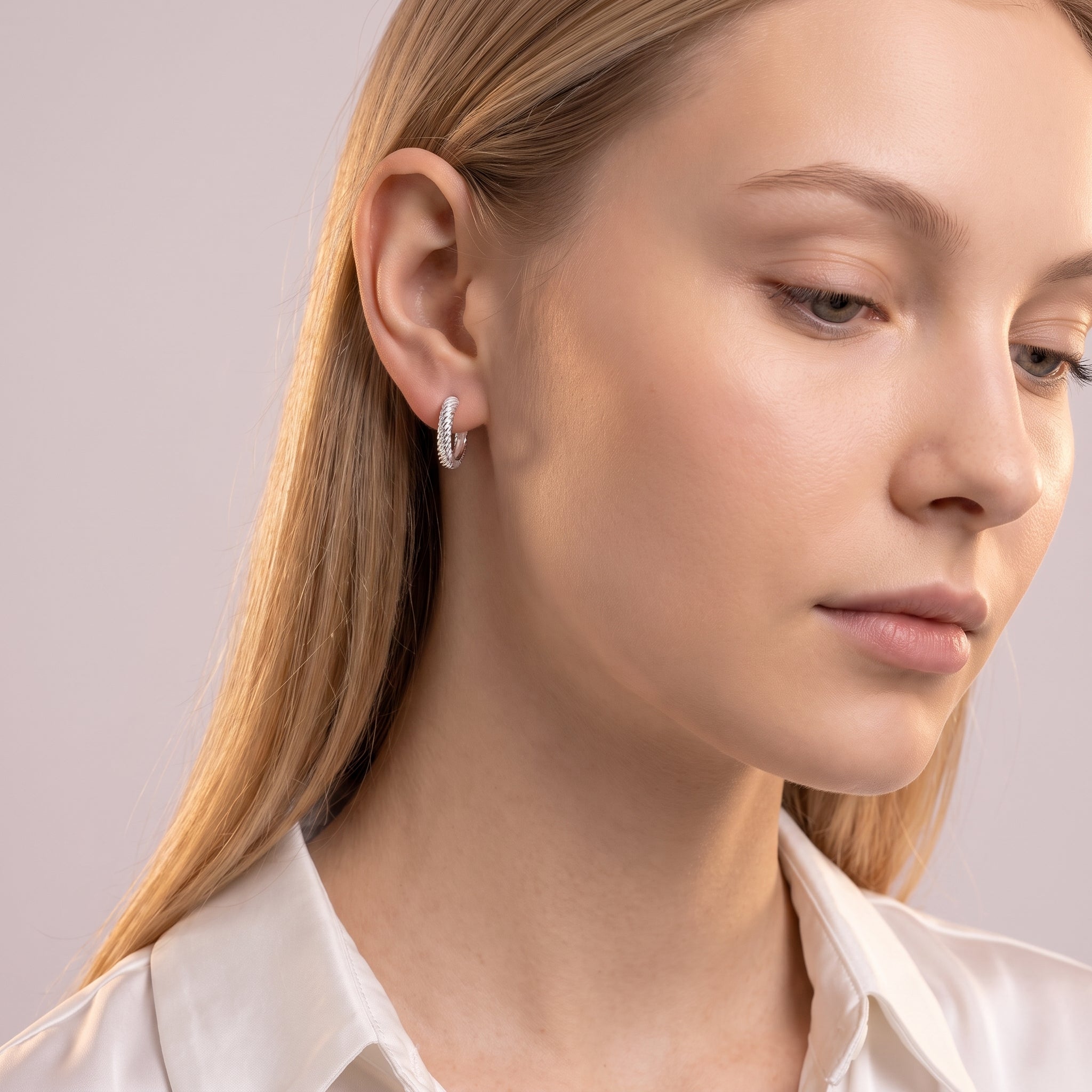 Silver rope huggie earring worn with the head tilted down