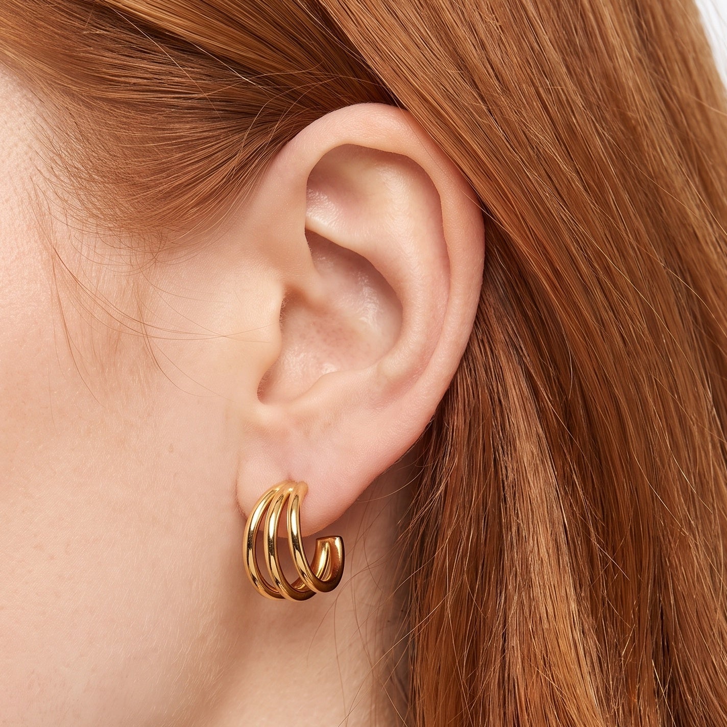 Gold triple hoop earrings hugging the earlobe in close-up