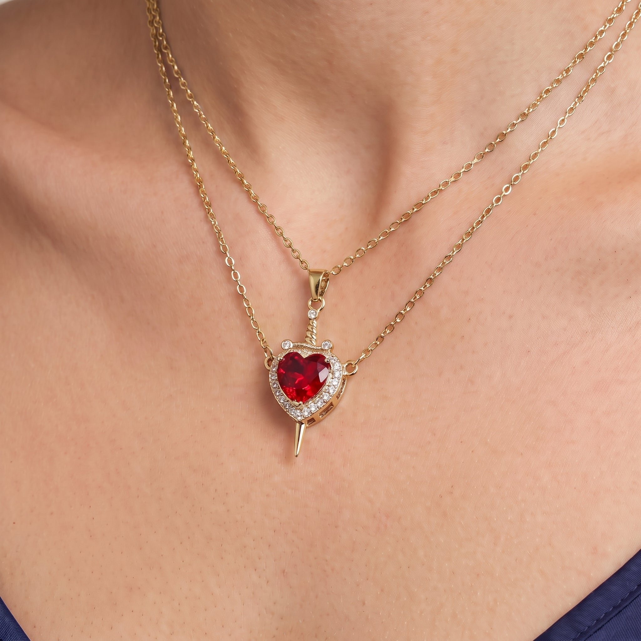 Gold heart and sword necklace, close-up of the red heart on skin