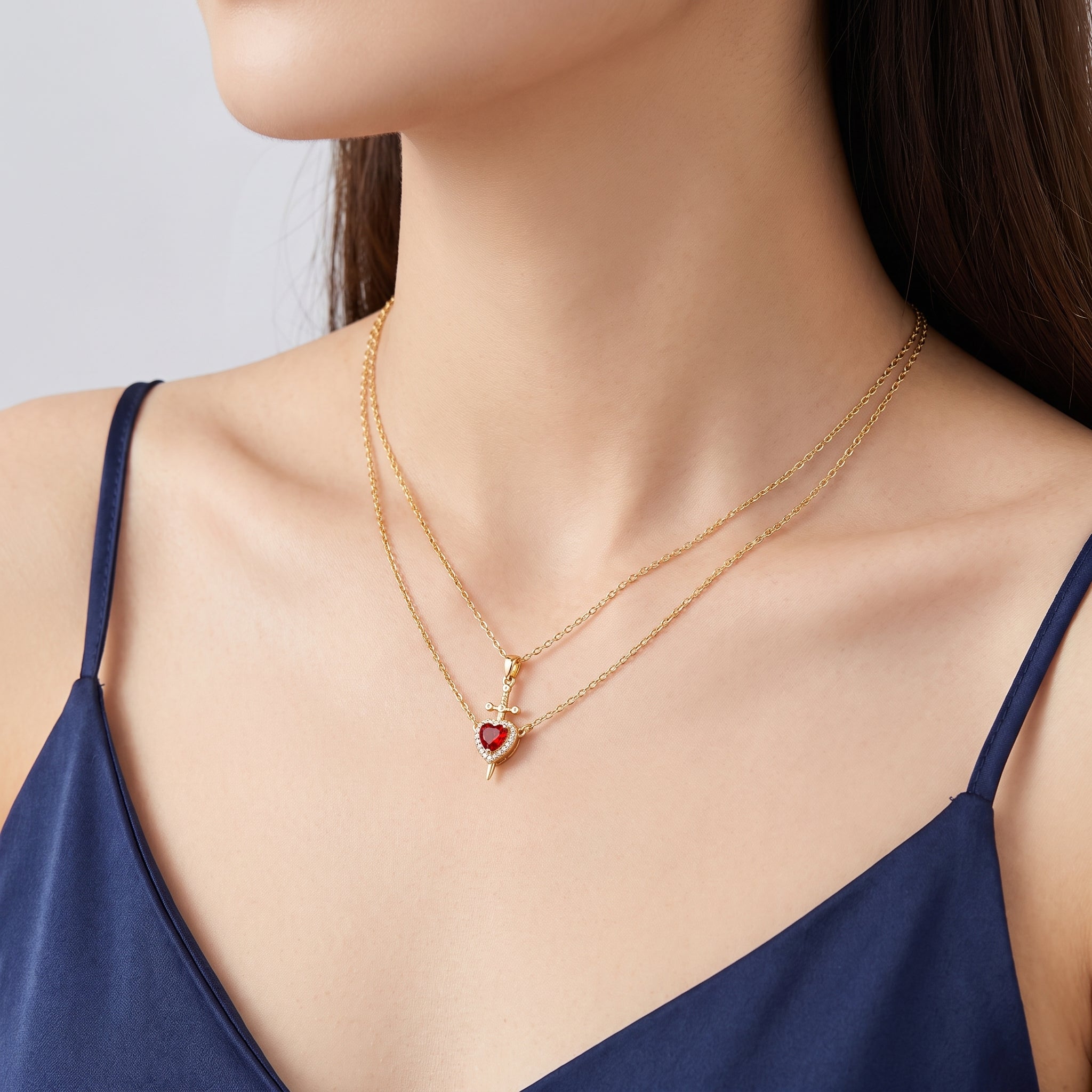 Gold heart and sword necklace at the collarbone, a navy camisole
