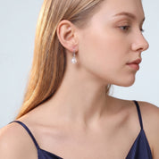 Blonde woman in navy camisole wearing Sabine pearl drop earring on pale blue-grey