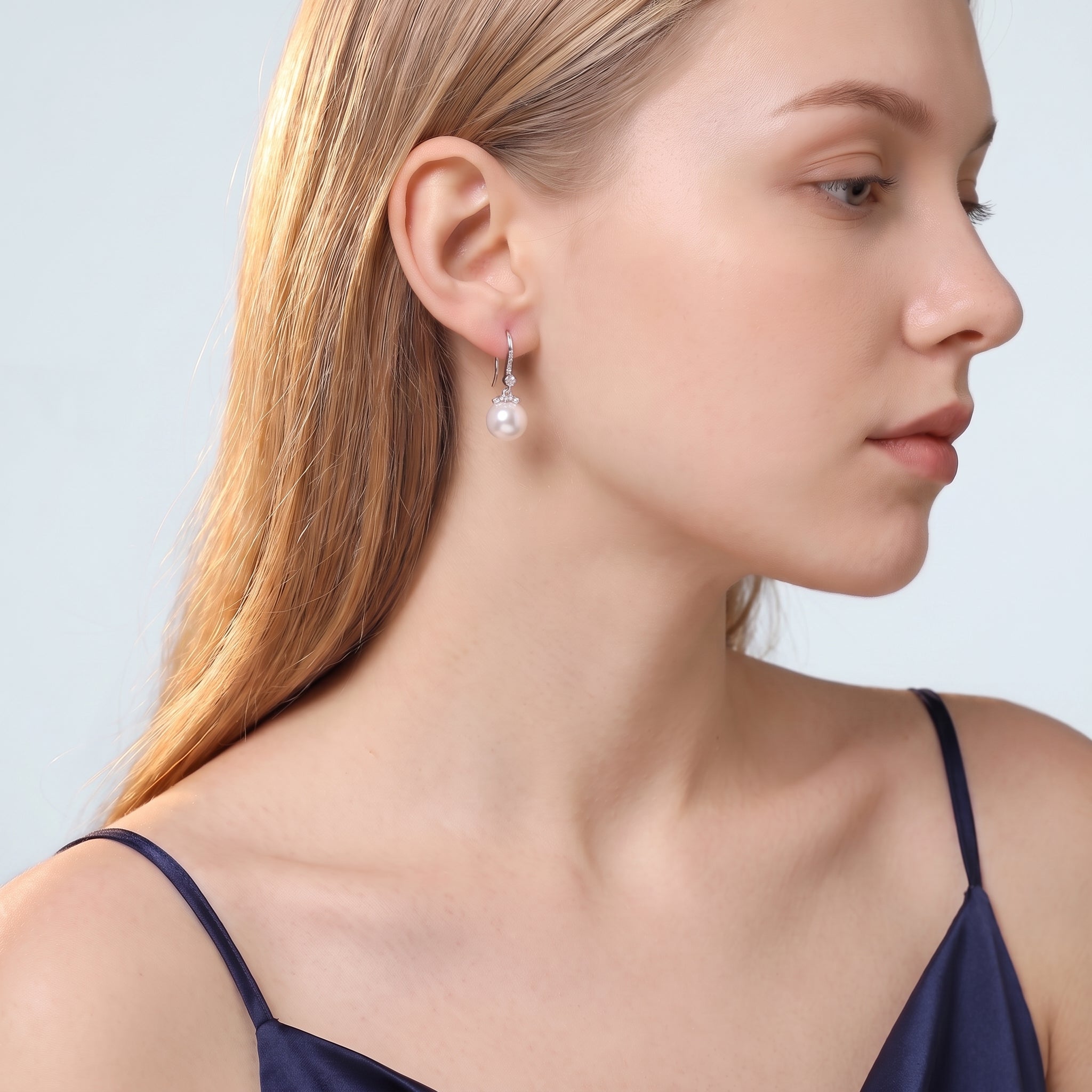 Blonde woman in navy camisole wearing Sabine pearl drop earring on pale blue-grey