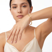 Gold twisted bangle on a raised wrist with a cream cami