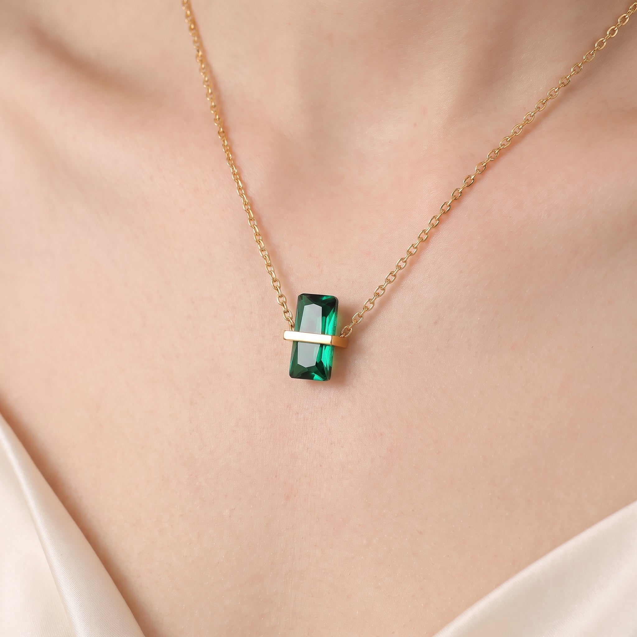 Close-up of the gold birthstone necklace's green crystal on the skin