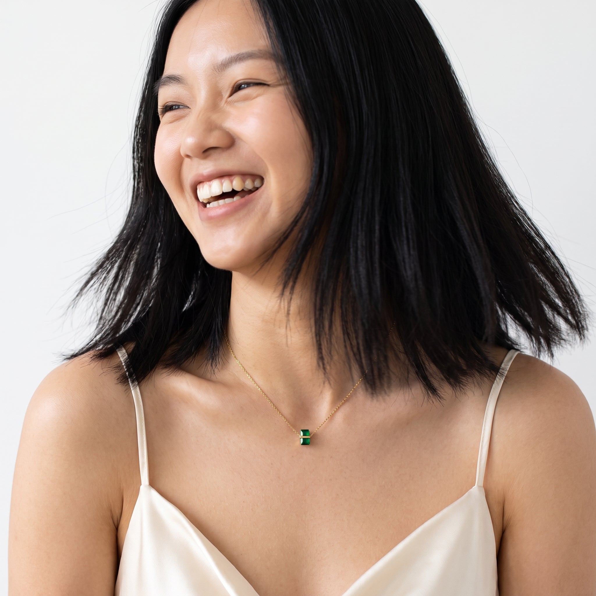 Gold birthstone necklace with a green crystal worn while laughing
