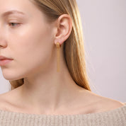 Gold tassel earring worn with an off-the-shoulder knit sweater