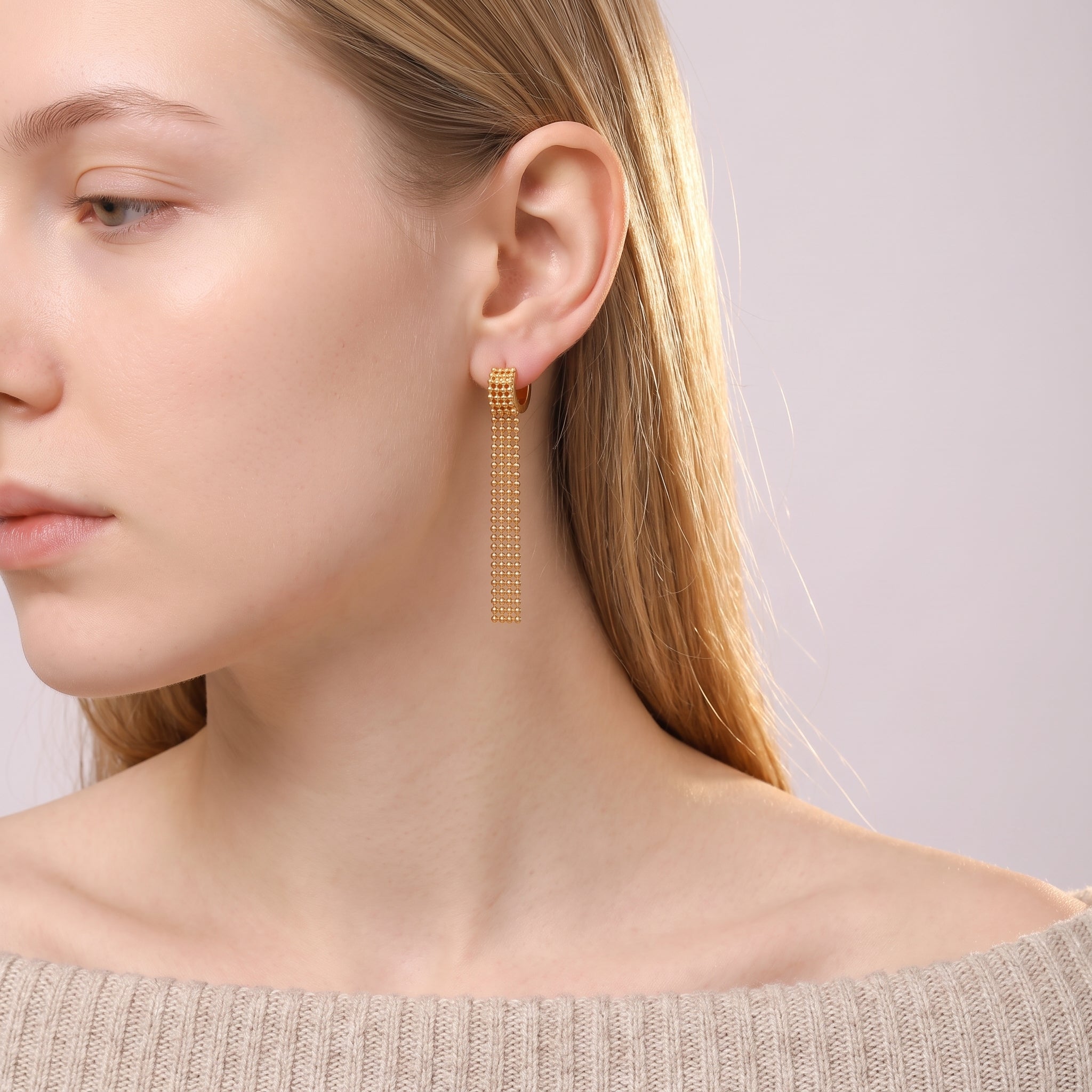 Gold tassel earring worn with an off-the-shoulder knit sweater