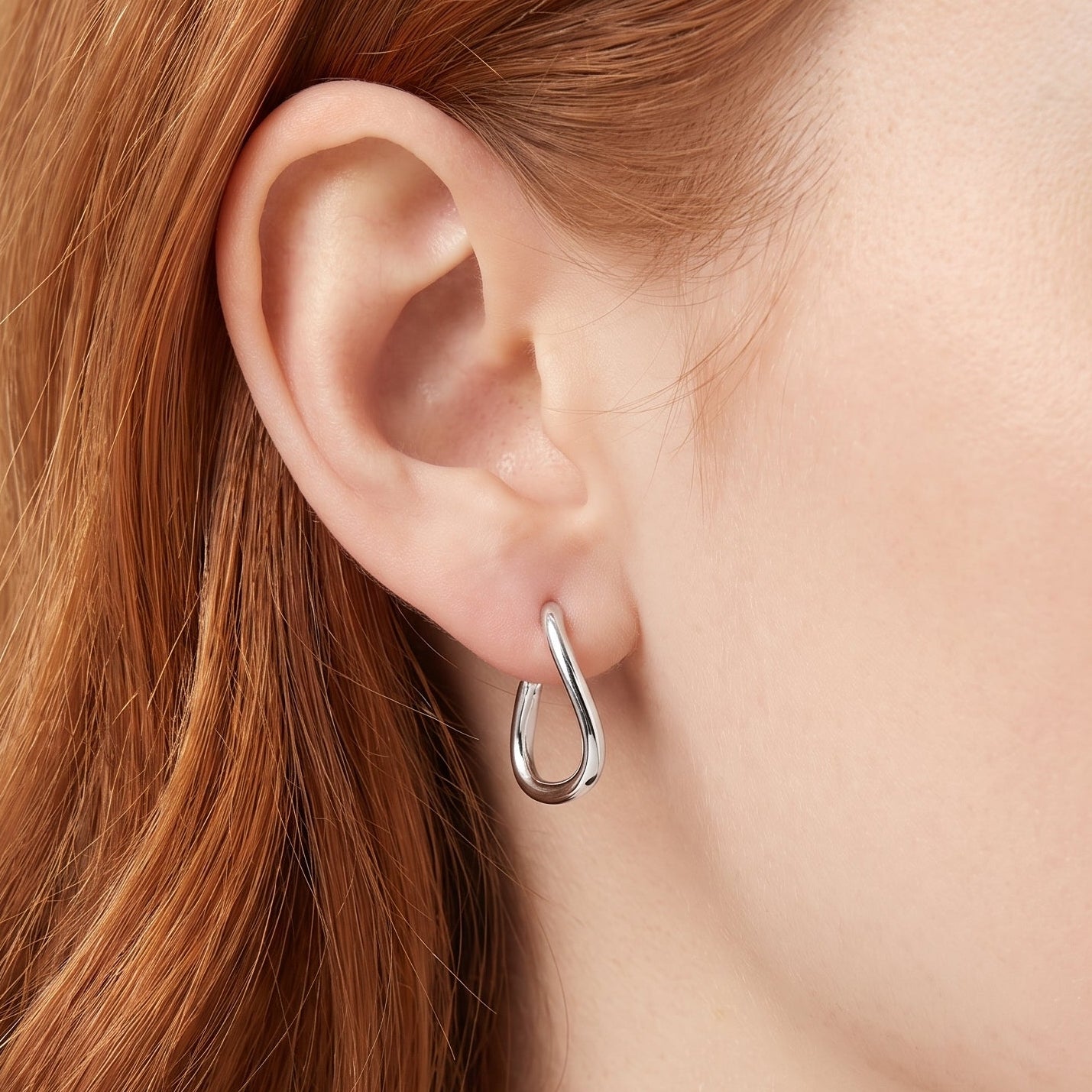Silver twisted teardrop hoop earring worn on the earlobe, close-up