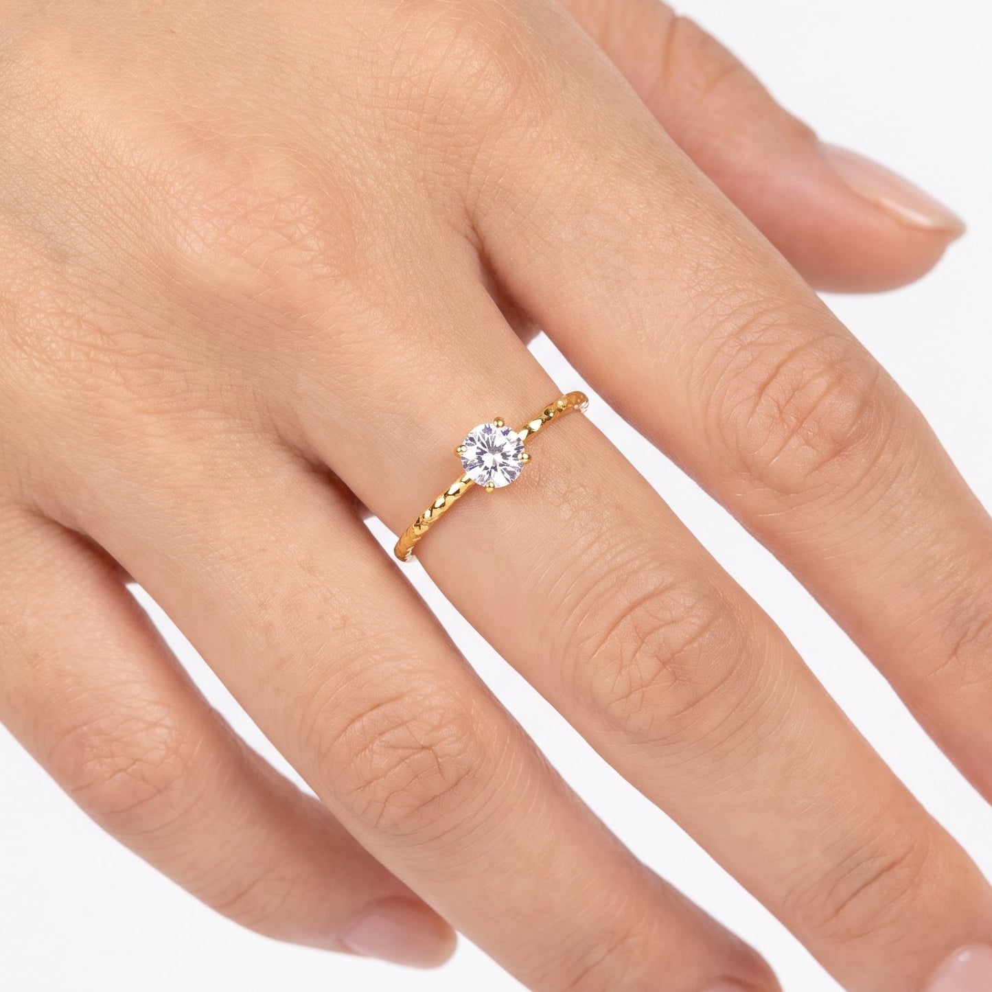 Gold solitaire ring with a round crystal on a hand