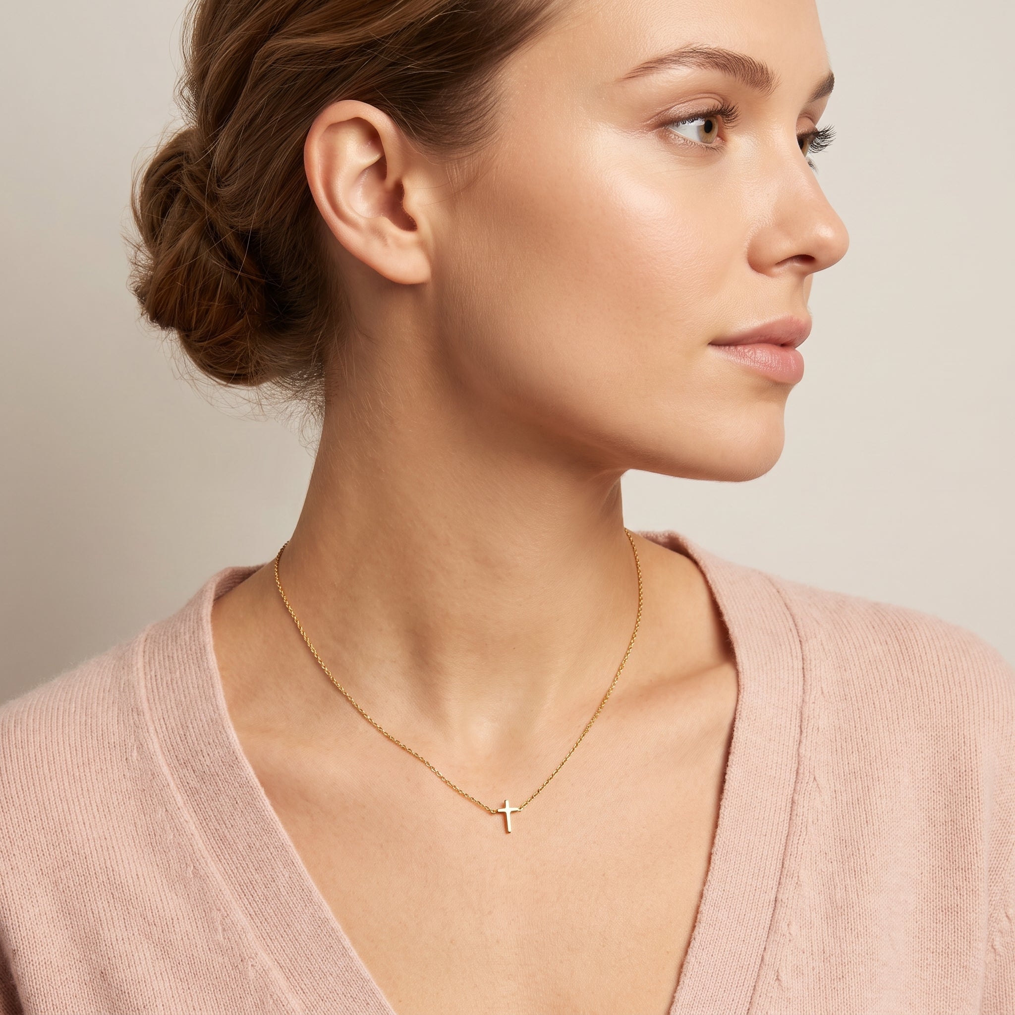 Gold tiny cross necklace worn in a shoulder-forward profile
