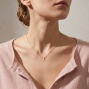 Gold tiny cross necklace worn, seen from a low angle