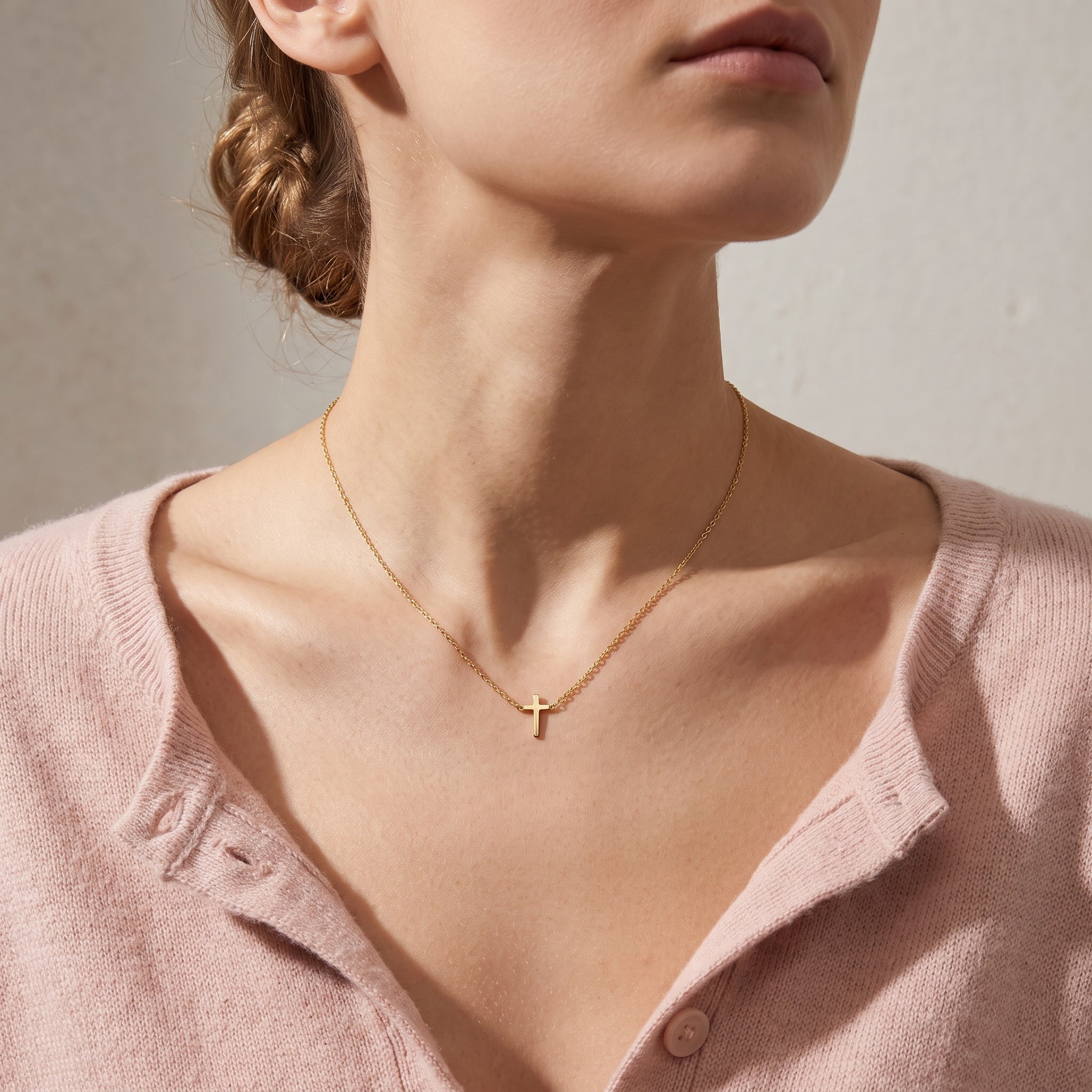 Gold tiny cross necklace worn, seen from a low angle