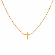 Gold tiny cross necklace laid out on a white background