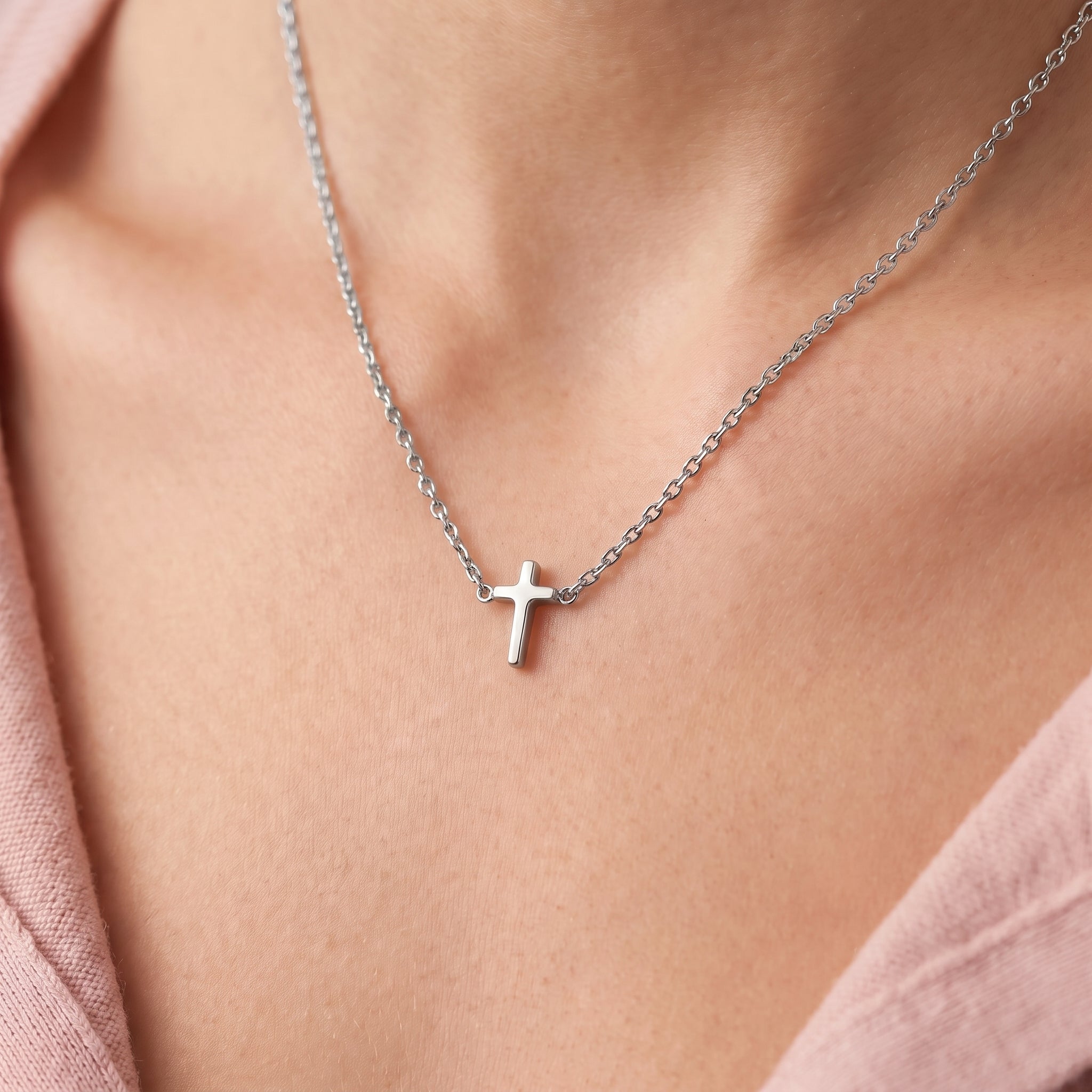 Silver tiny cross necklace, close-up of the polished cross on skin