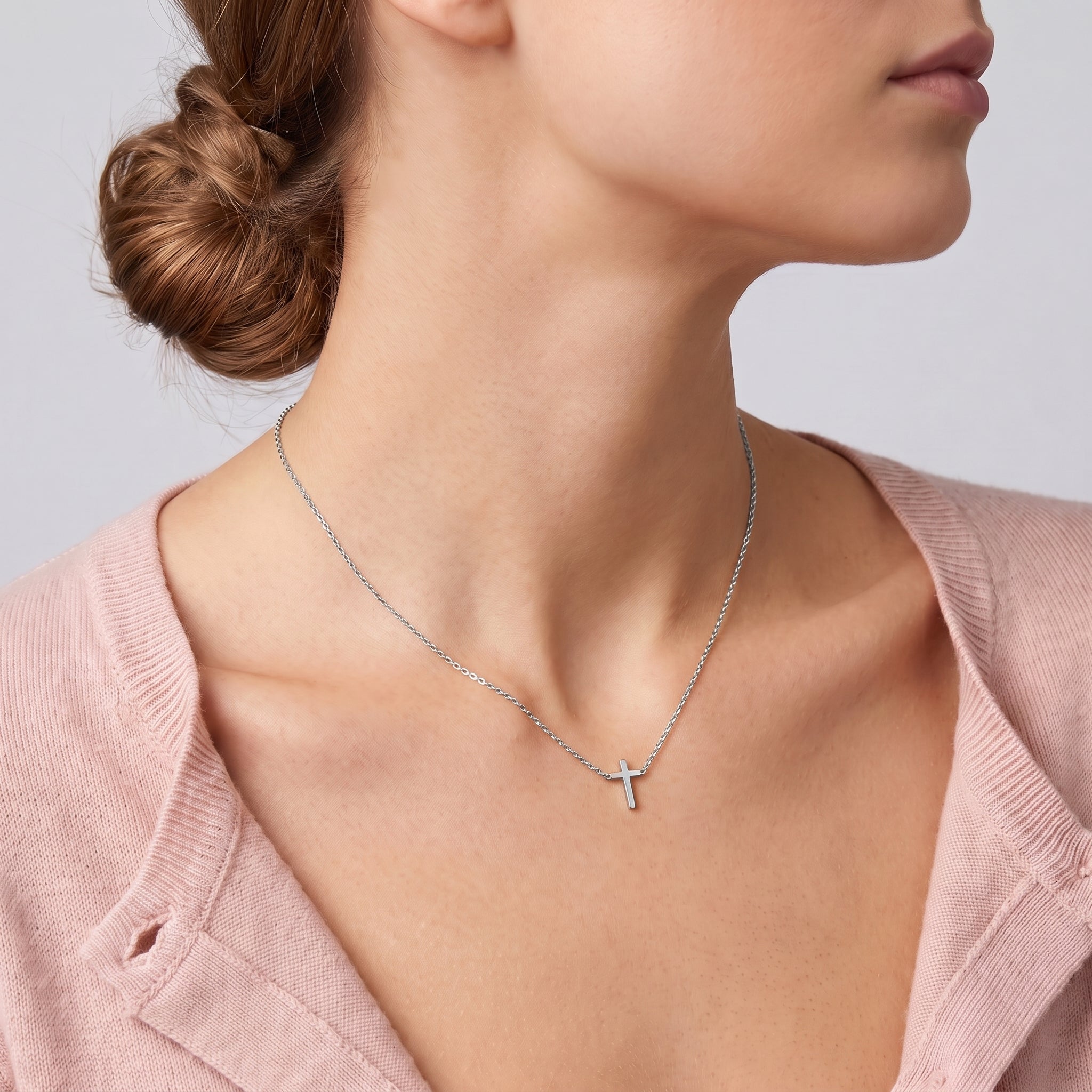 Silver tiny cross necklace at the collarbone, a blush cardigan