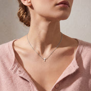 Silver tiny cross necklace worn, seen from a low angle