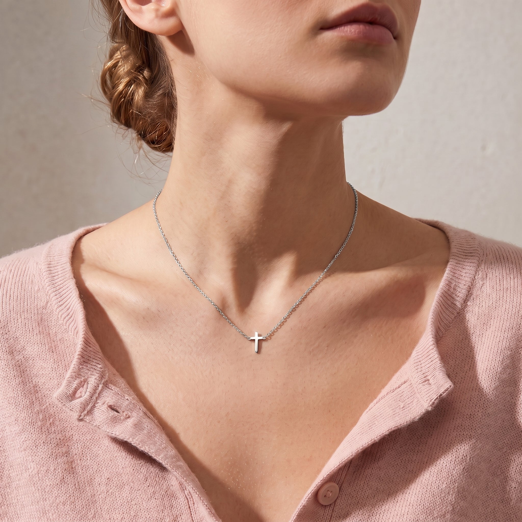 Silver tiny cross necklace worn, seen from a low angle