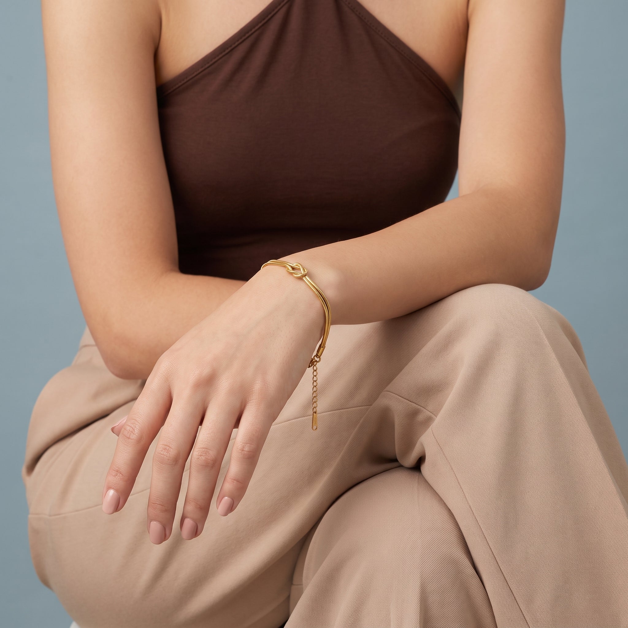 Gold love knot bracelet worn with the forearm on the knee