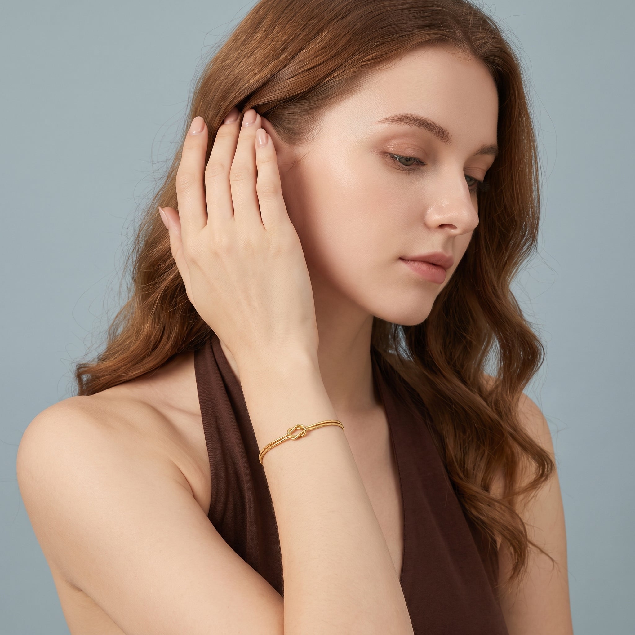 Gold love knot bracelet worn with a hand raised to the hair