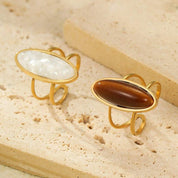 Two gold-rimmed rings with stone inlays on a beige surface